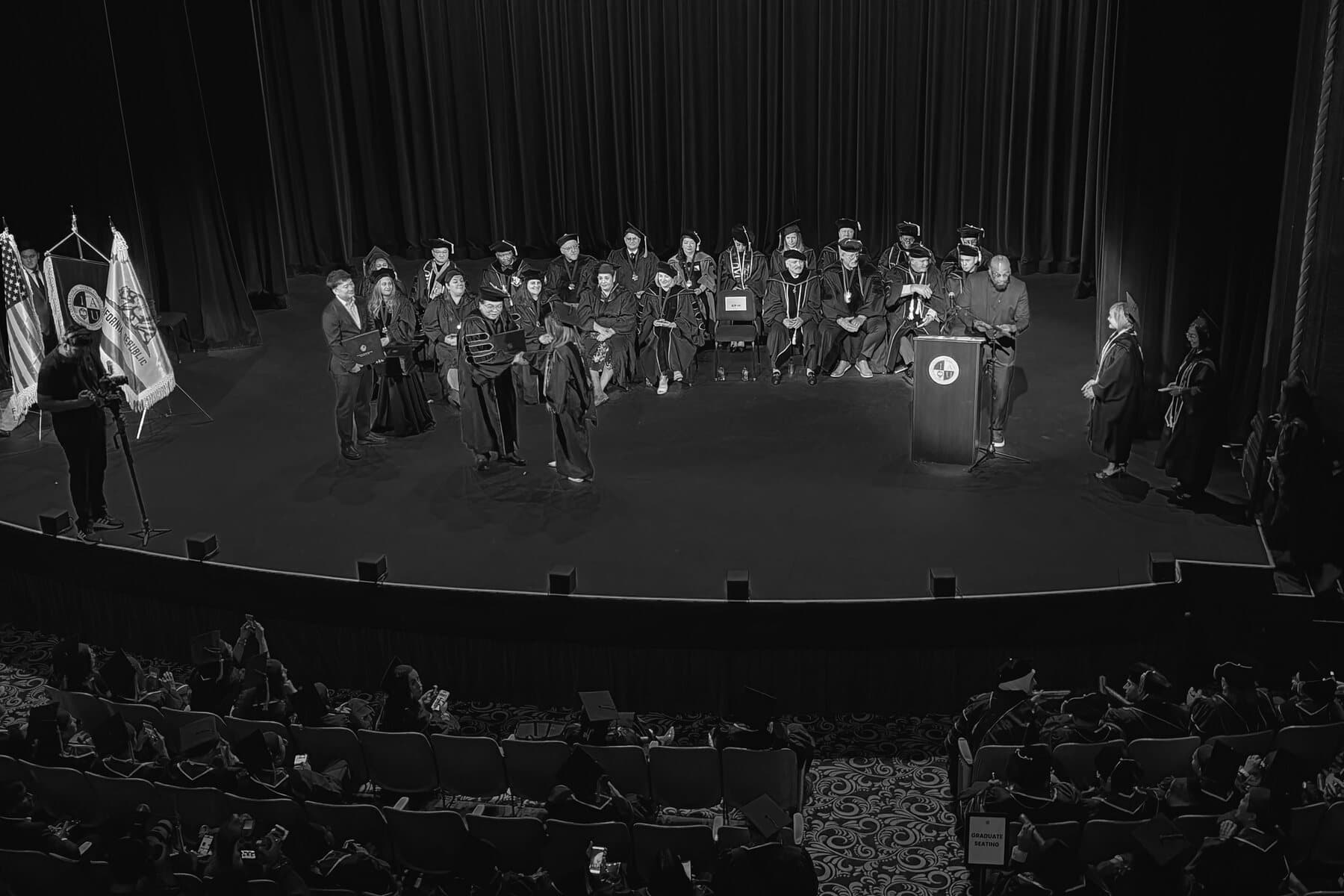 The 2026 commencement stage at the Orpheum, Los Angeles, seen from the hall — graduates seated in a row before the flags