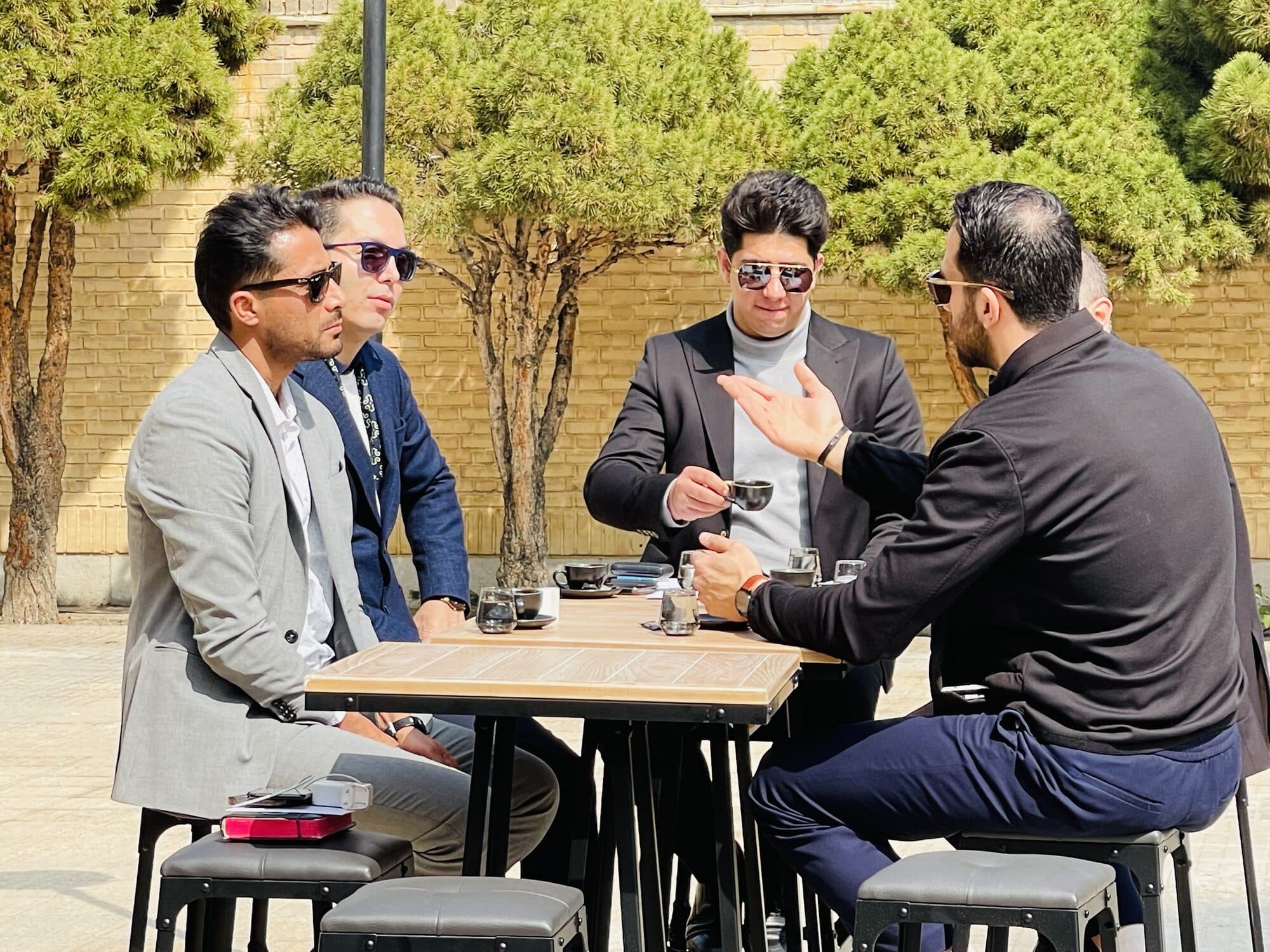 Four men in conversation around a standing table in the courtyard