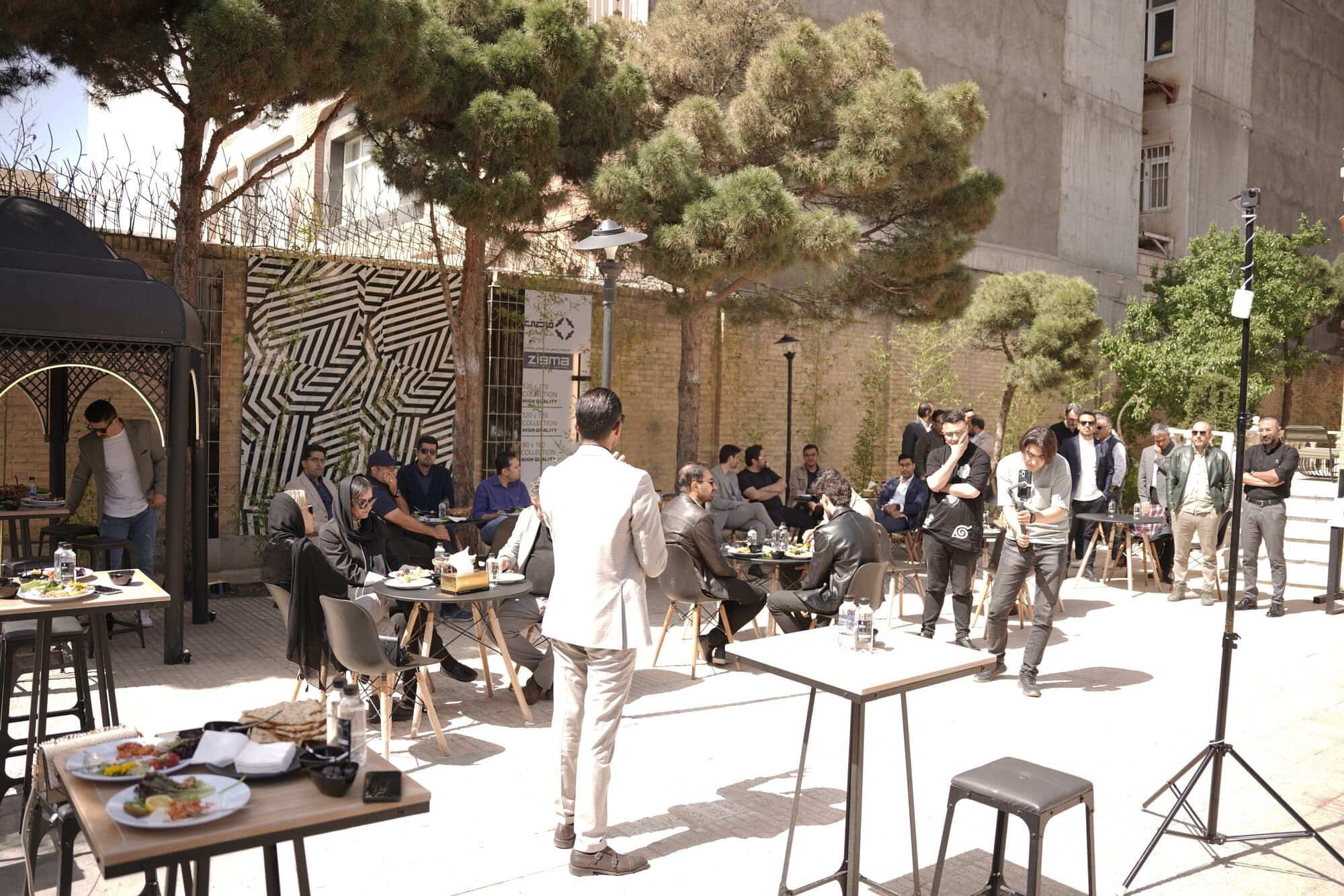 A working breakfast in the HAYAT courtyard — tables laid under the pines, the industry seated, one guest standing to speak
