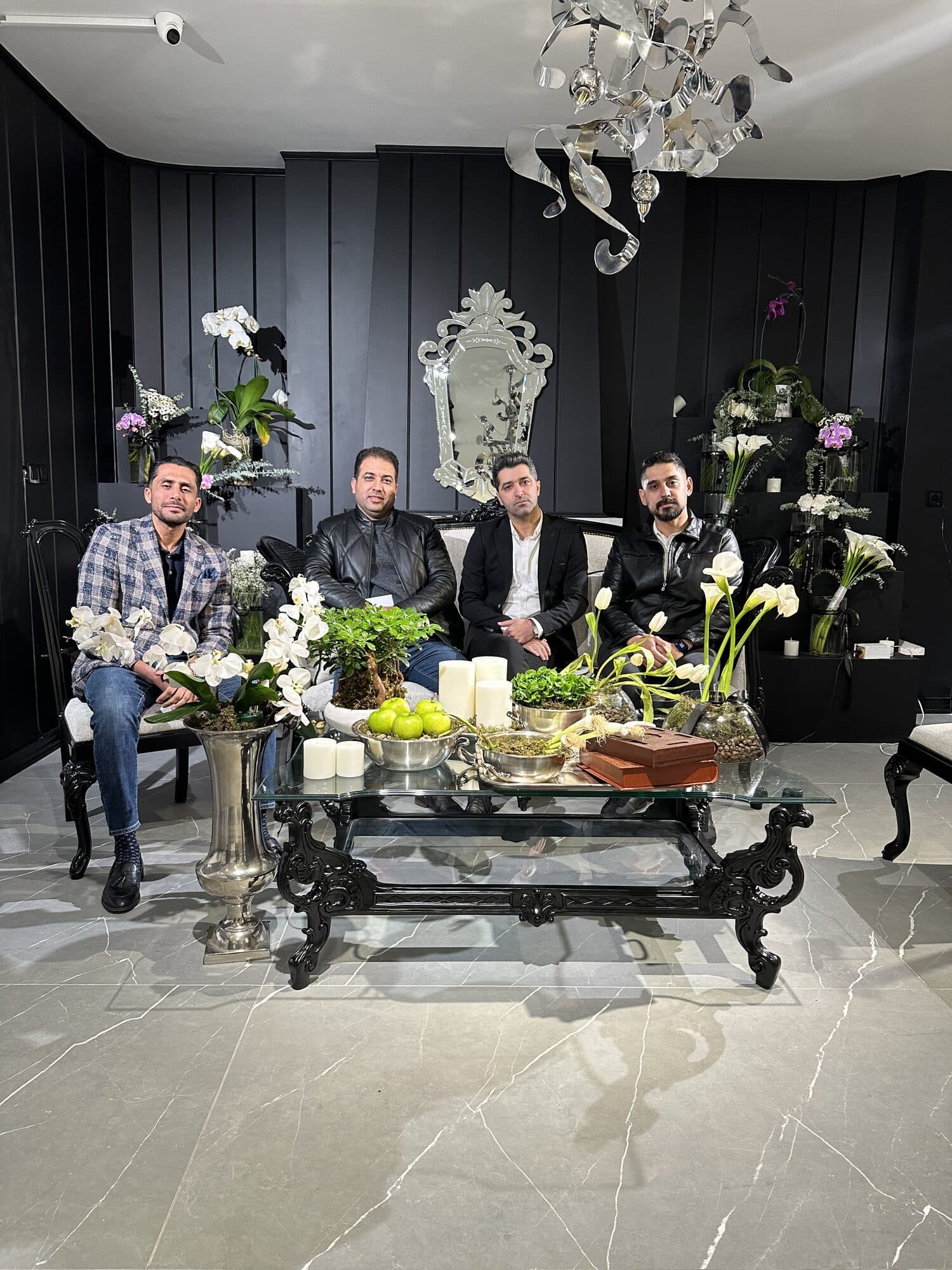 Four members seated around a glass table in the dark-panelled lounge, orchids and candles laid out between them under a cut-glass chandelier