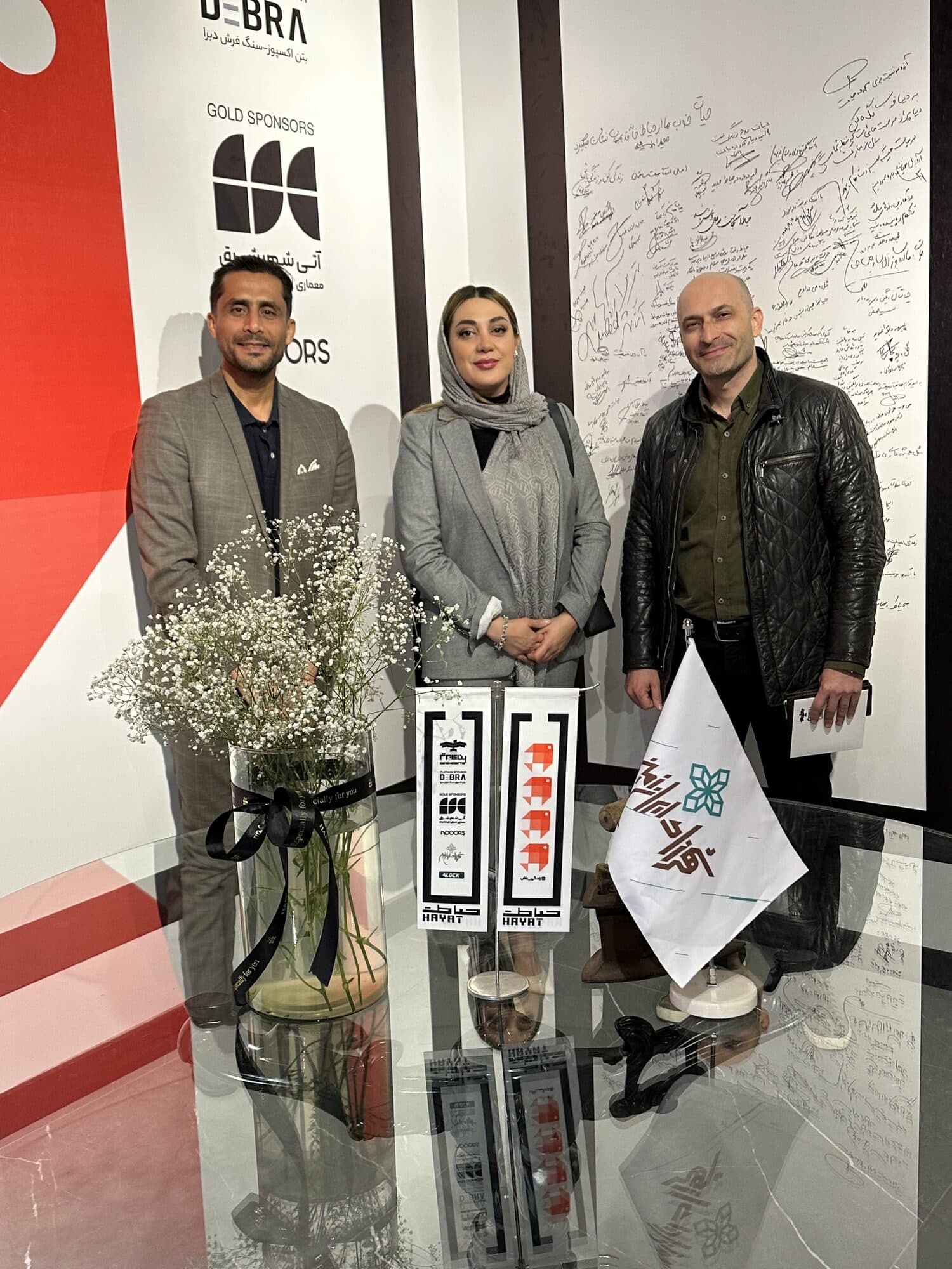 Three members photographed at the signed wall, the sponsor board and the HAYAT pennant beside them