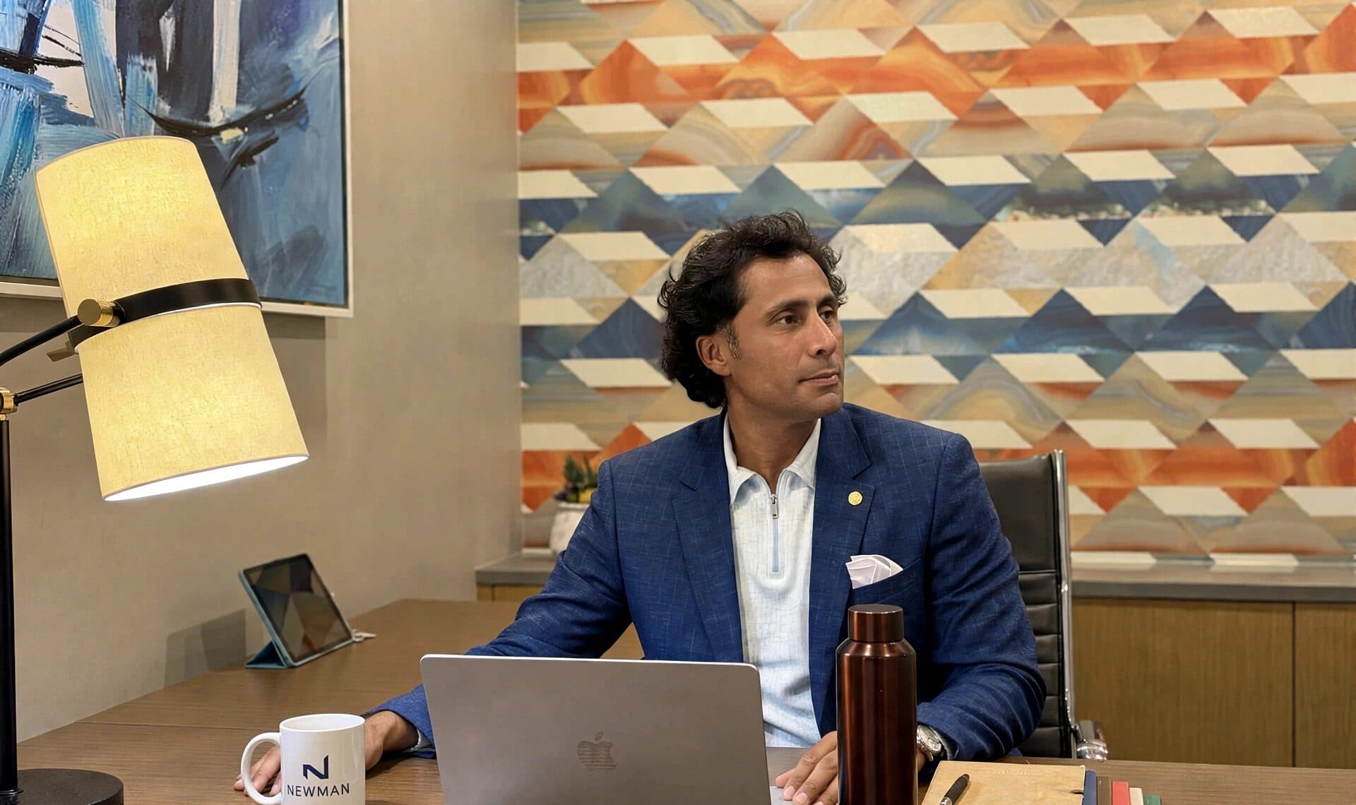 Ehsan Kaykhah at a desk in a Los Angeles office, laptop open, NEWMAN mug beside it.