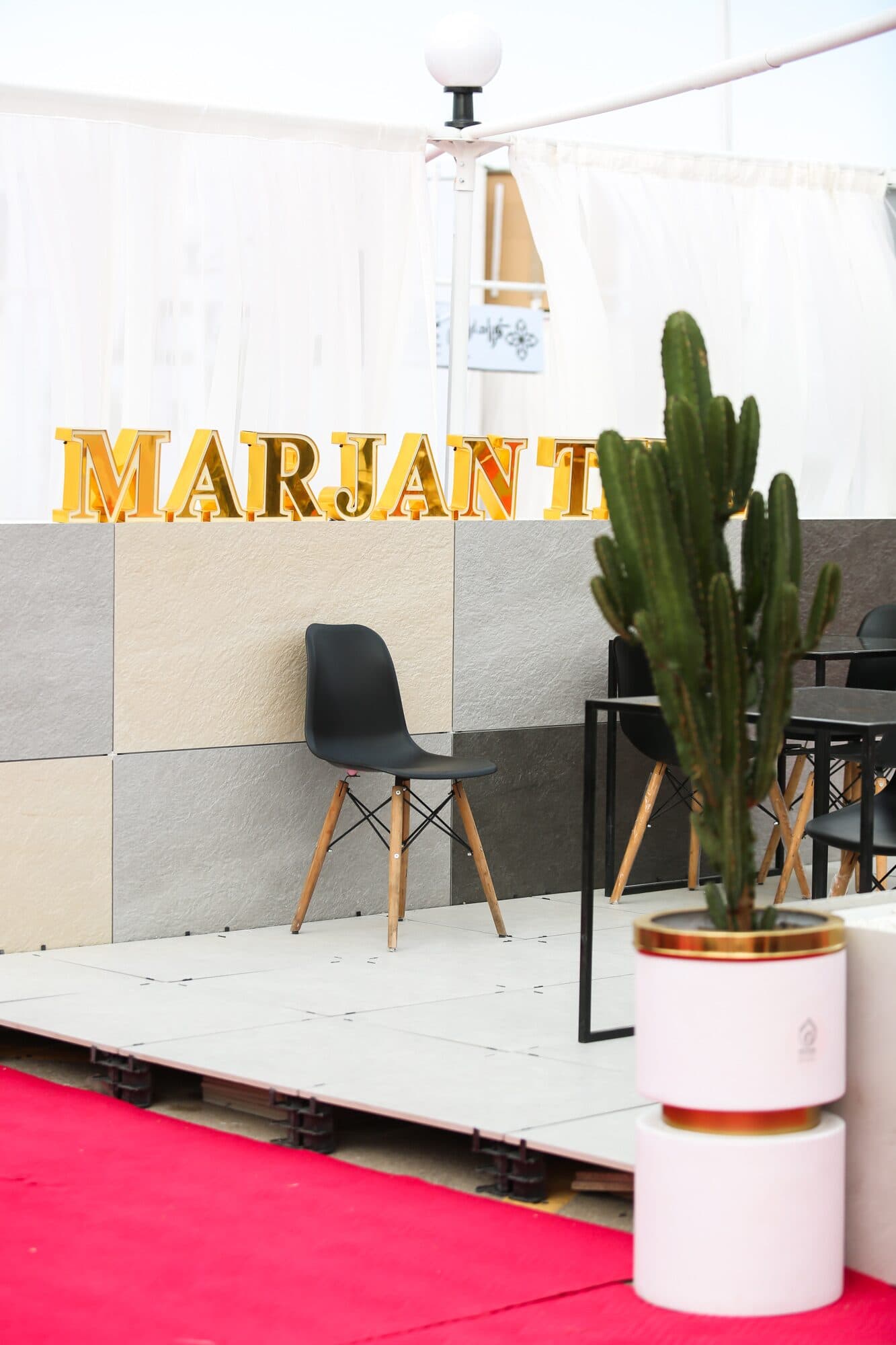 The Marjan Tile setting — a lit wordmark over tiled walls, a single chair and a cactus in a drum planter