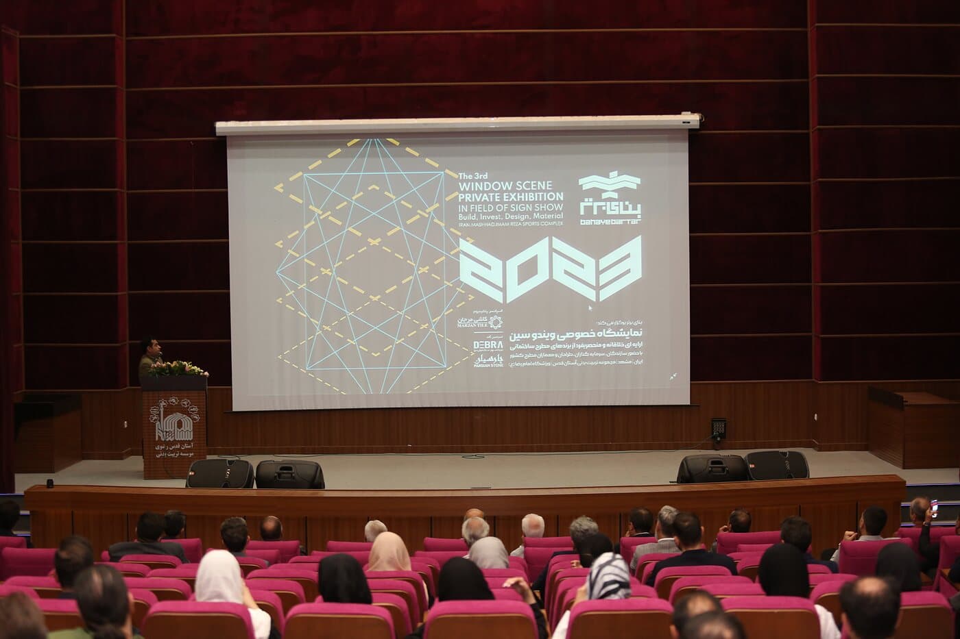 A full auditorium facing the Banaye Bartar programme on screen, Mashhad