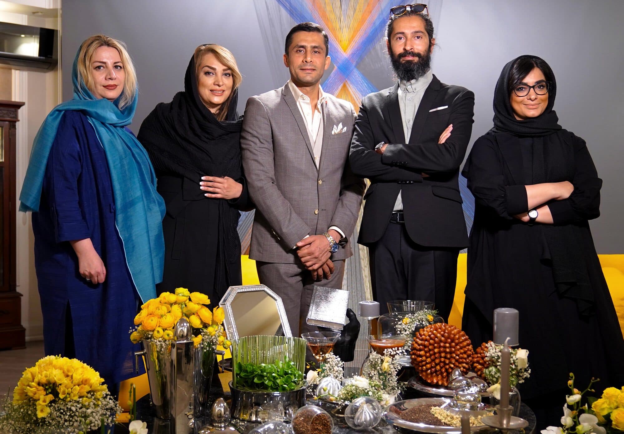 پنج مهمان کنار هم، جلوی پس‌زمینه‌ی بافته‌ی آن شب، با سفره‌ی هفت‌سین چیده‌شده در پیش‌زمینه.