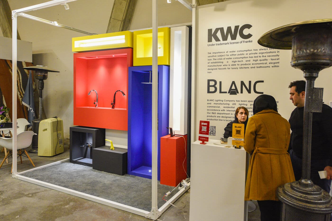 A setting in blocks of red, yellow and blue inside a white frame, visitors reading the panel beside it