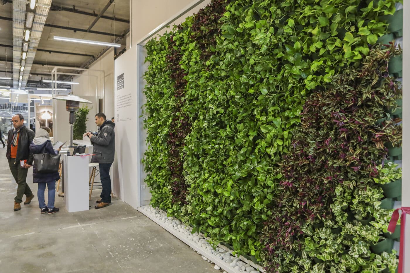A living green wall running the length of the concrete hall, visitors alongside it