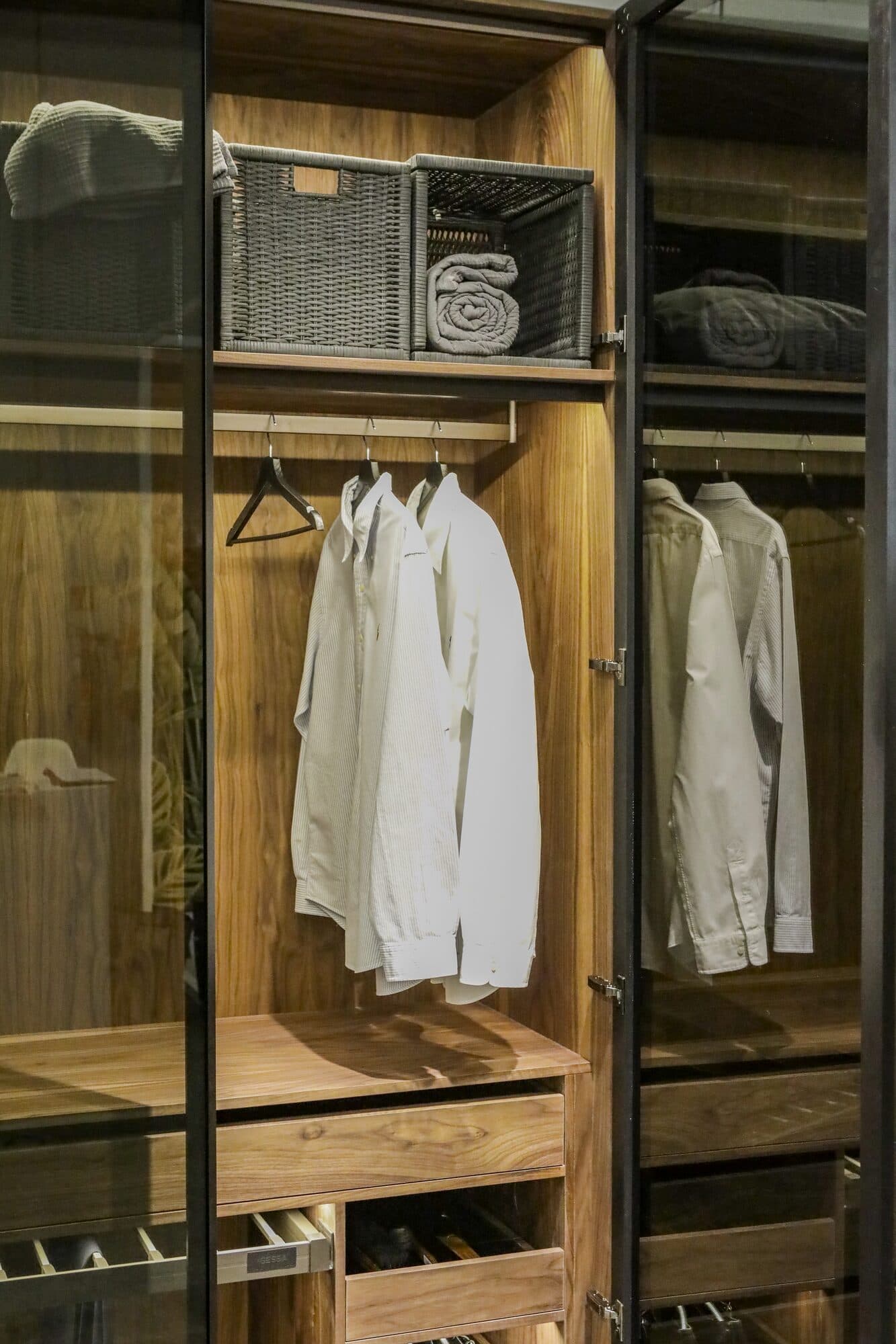 An open wardrobe setting in oak and steel, shirts hung in a lit bay