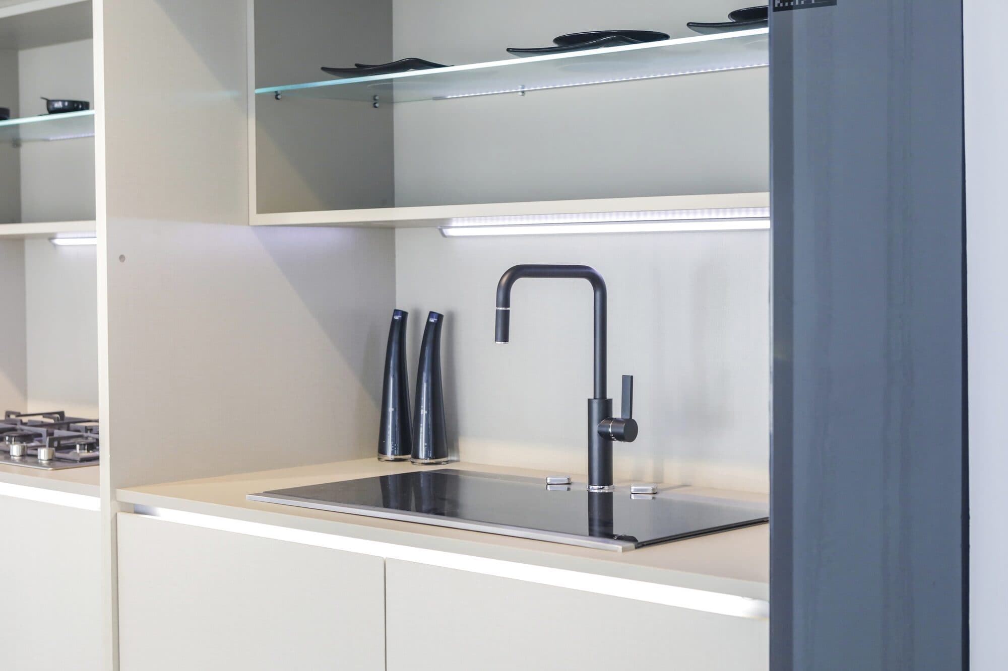 A white kitchen setting with a single black tap and open shelving