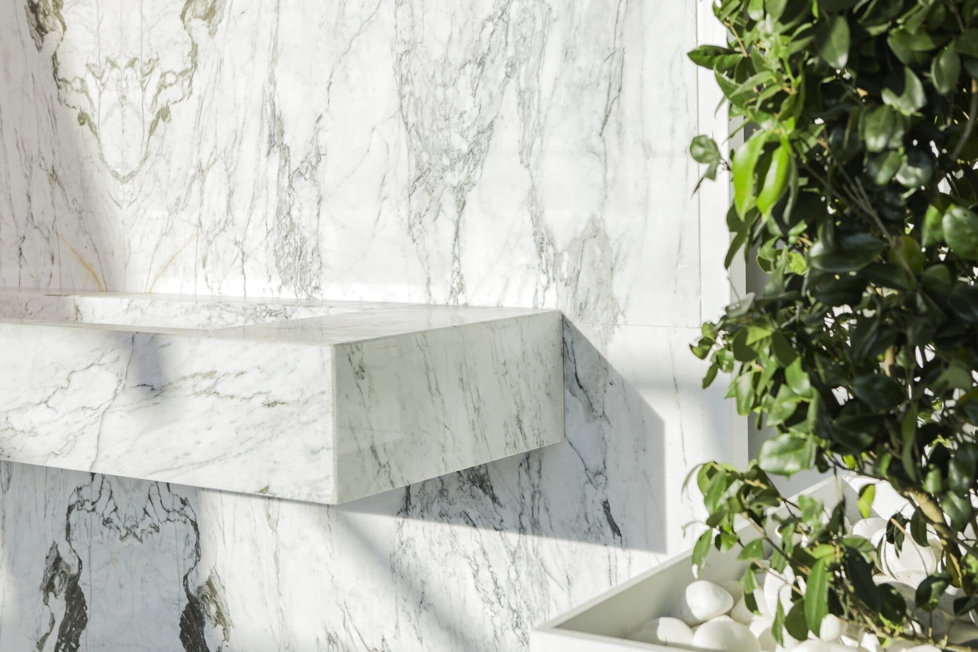A marble bench cantilevered from a book-matched marble wall, planting spilling down beside it