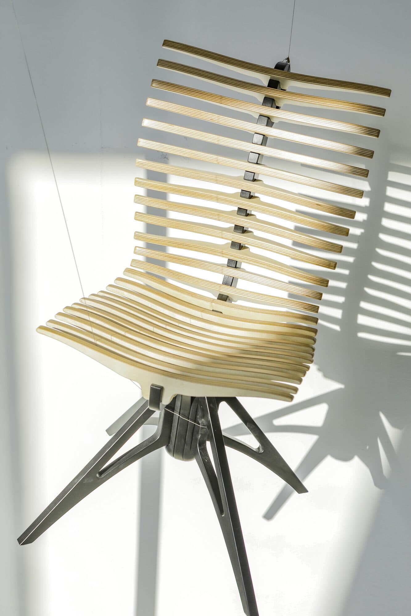 A slatted timber chair on a black tripod base, standing alone against a white wall