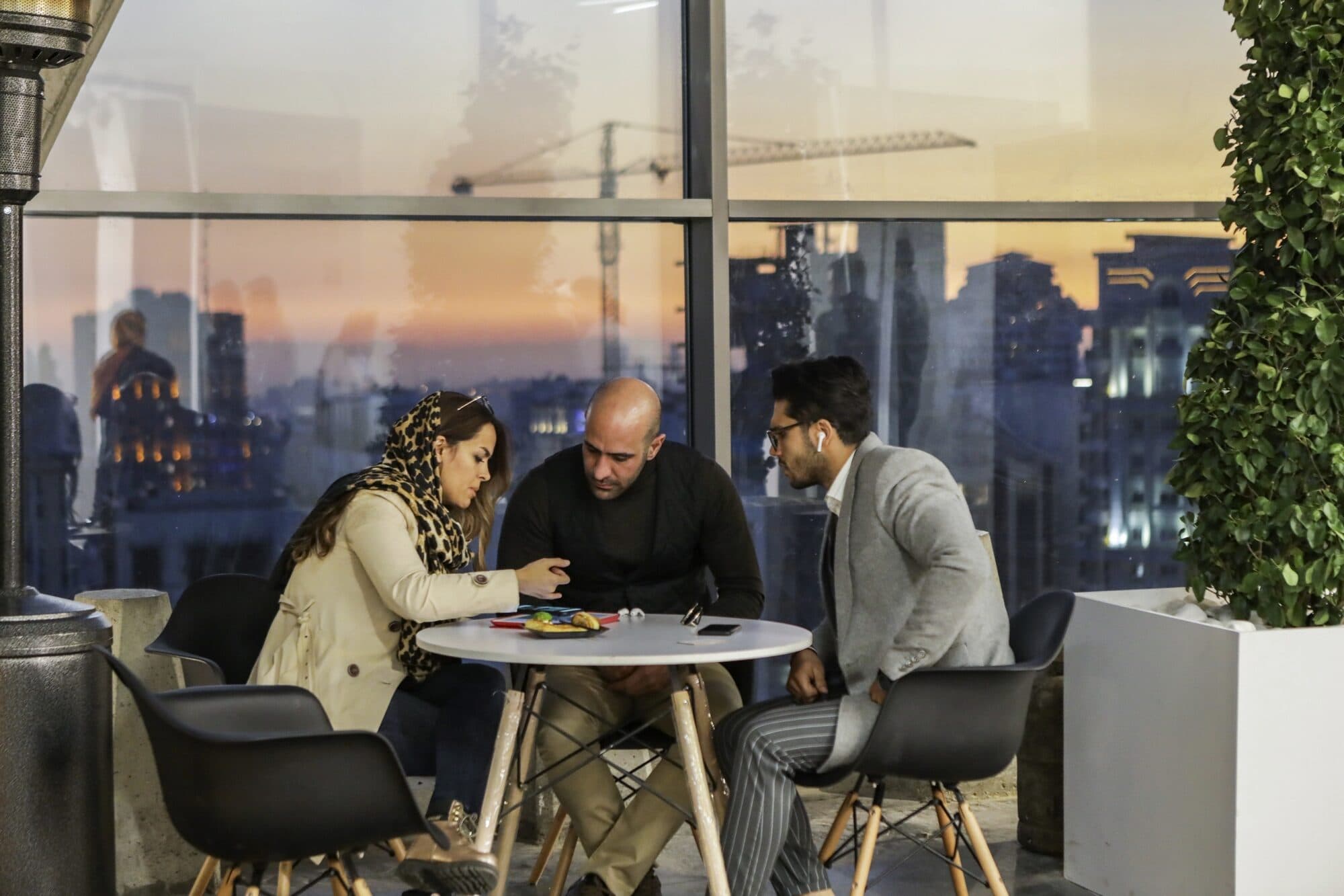 A table above the city on the terrace, three people mid-conversation at dusk