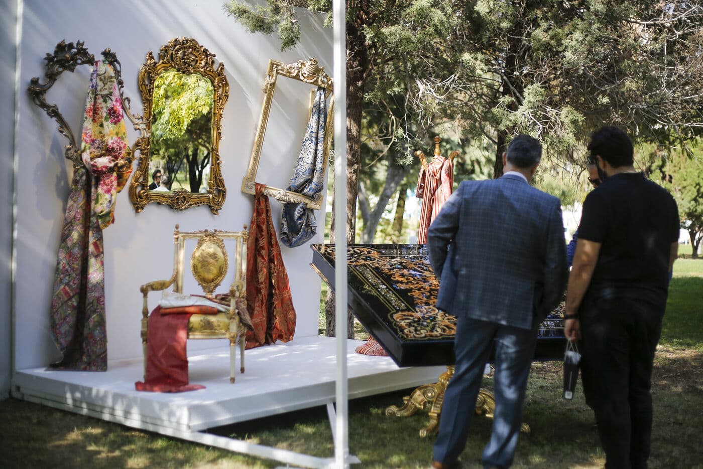 A setting of gilt mirrors and textiles staged in the open air, visitors passing through