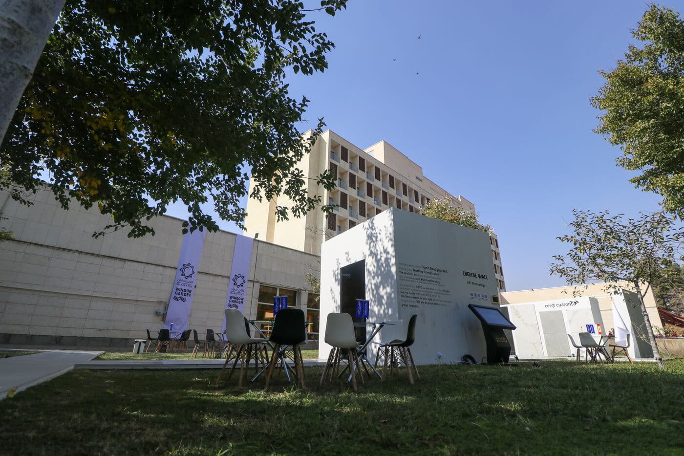 The edition seen whole: open lawn, trees and white pavilions under a clear sky
