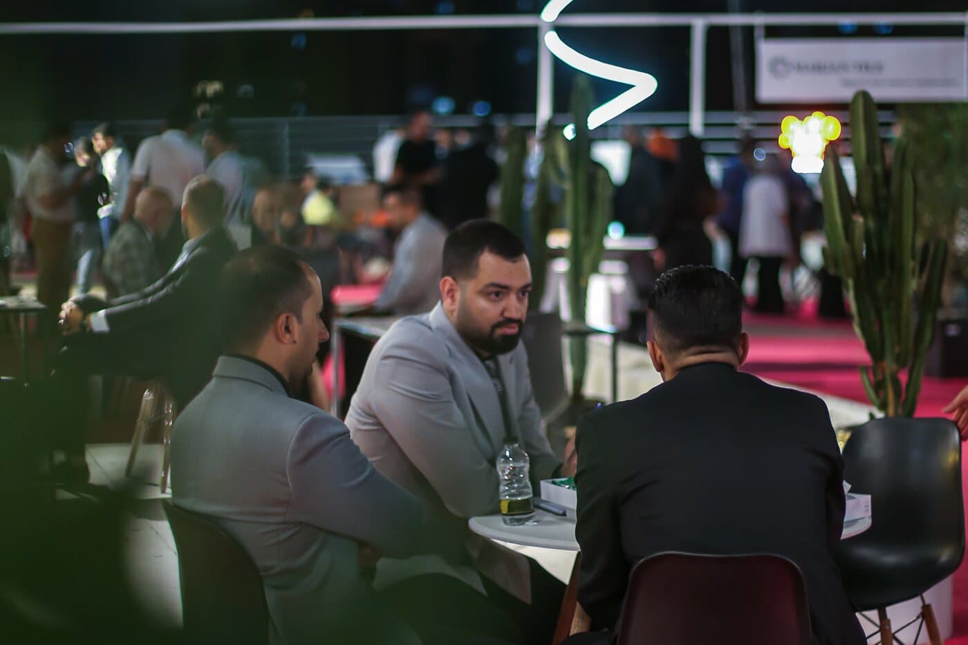 Members talking across café tables after dark, the edition still open around them