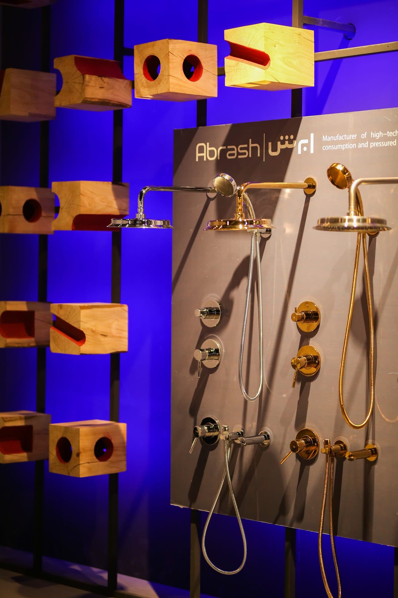Brass taps and showers mounted on timber blocks against a wall lit deep blue
