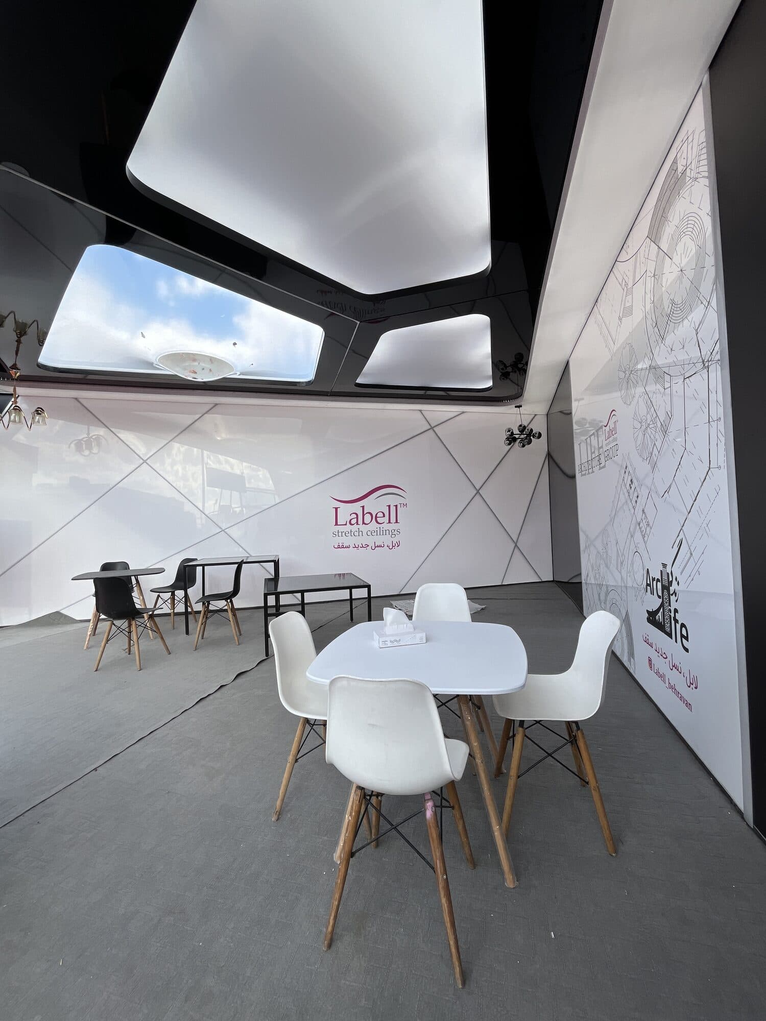A stand under a black canopy cut with skylights, a white table and chairs beneath it