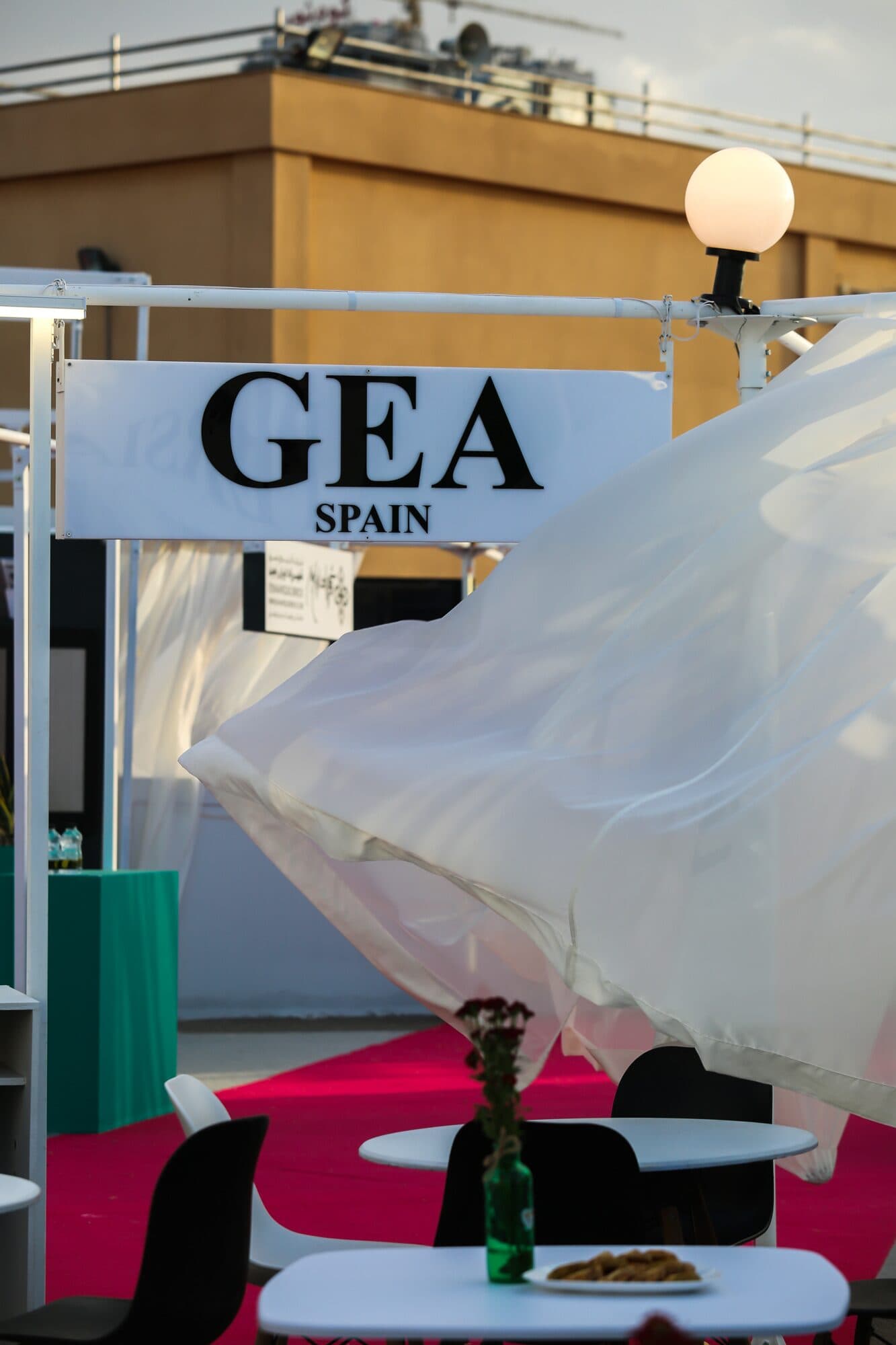 A white curtain lifting across the front of a stand, low tables laid behind it
