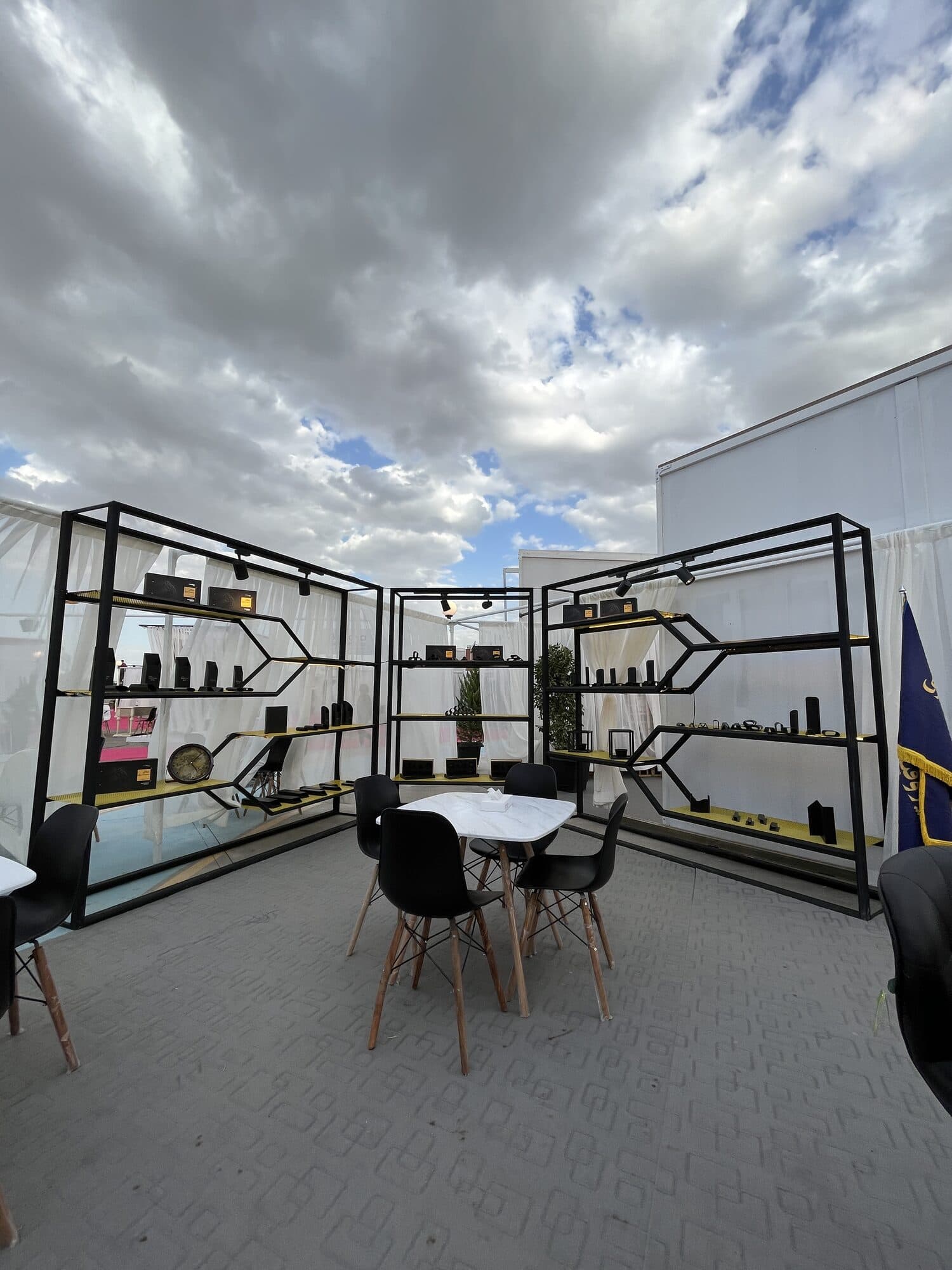 A pavilion of black steel shelving open on three sides, a table and chairs in its corner