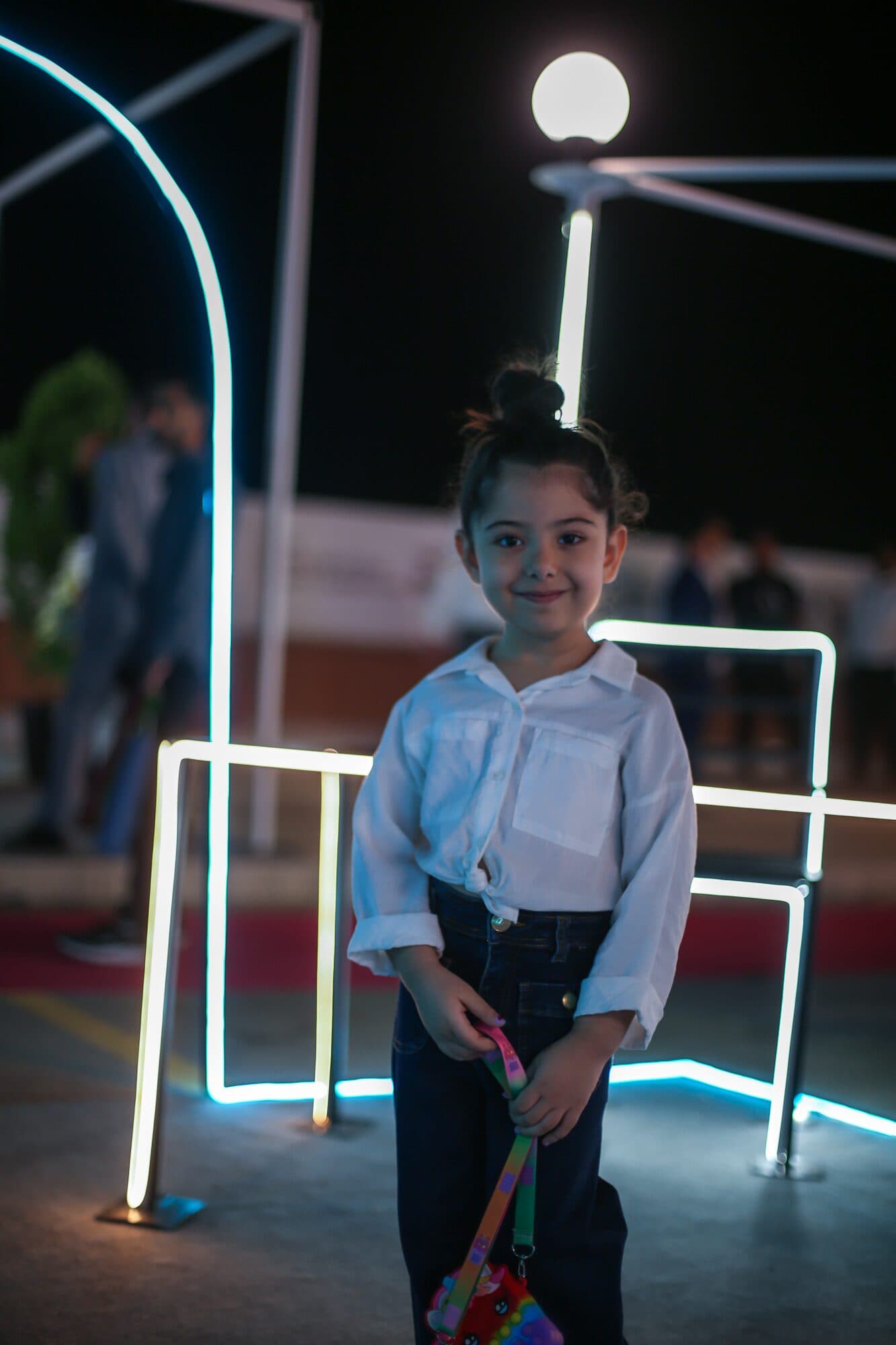 A child standing inside a lit neon arch on the red route after dark
