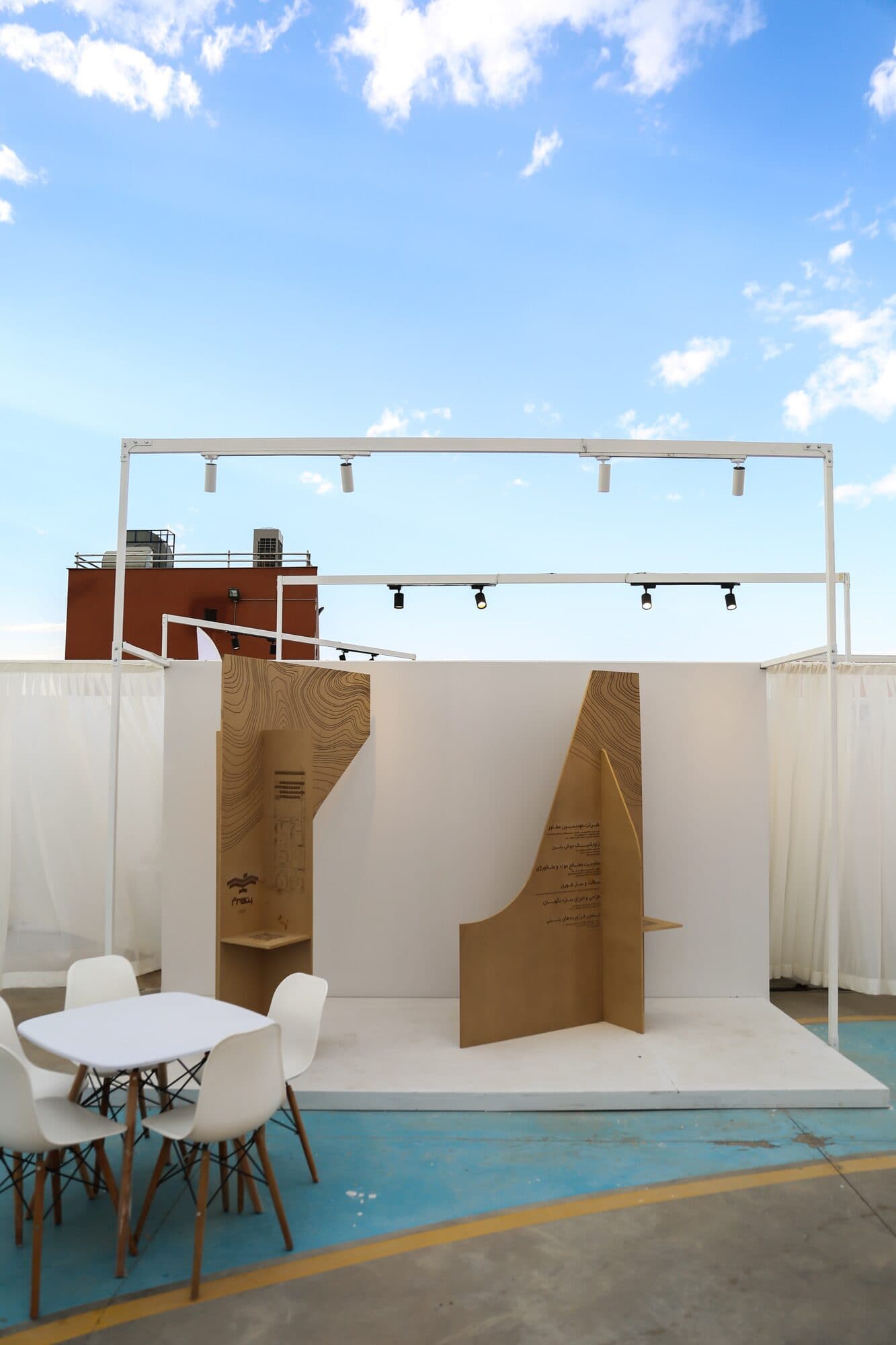 A stand of folded timber panels standing on a pale blue floor, café chairs alongside