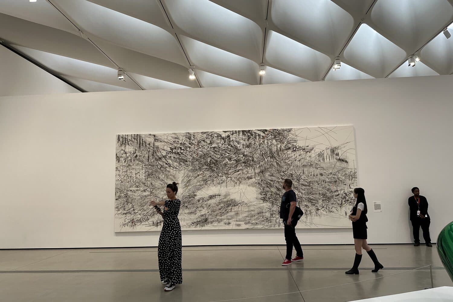 The top-floor gallery under the vaulted skylights, visitors spread out in front of one large work