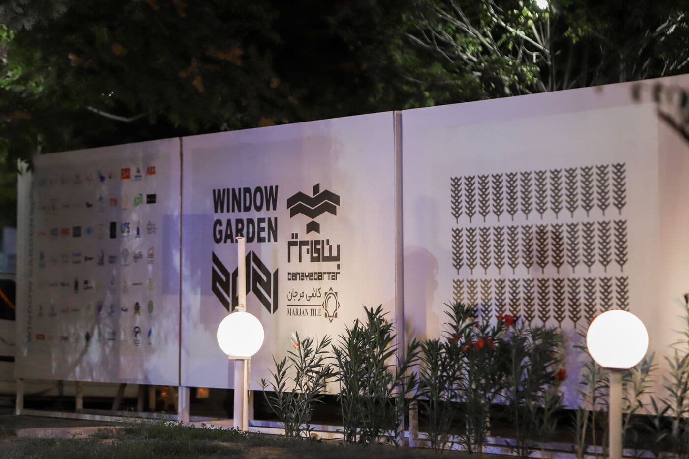 The entrance wall carrying the WINDOW GARDEN mark and the exhibitors' logos, at dusk — Mashhad 2021