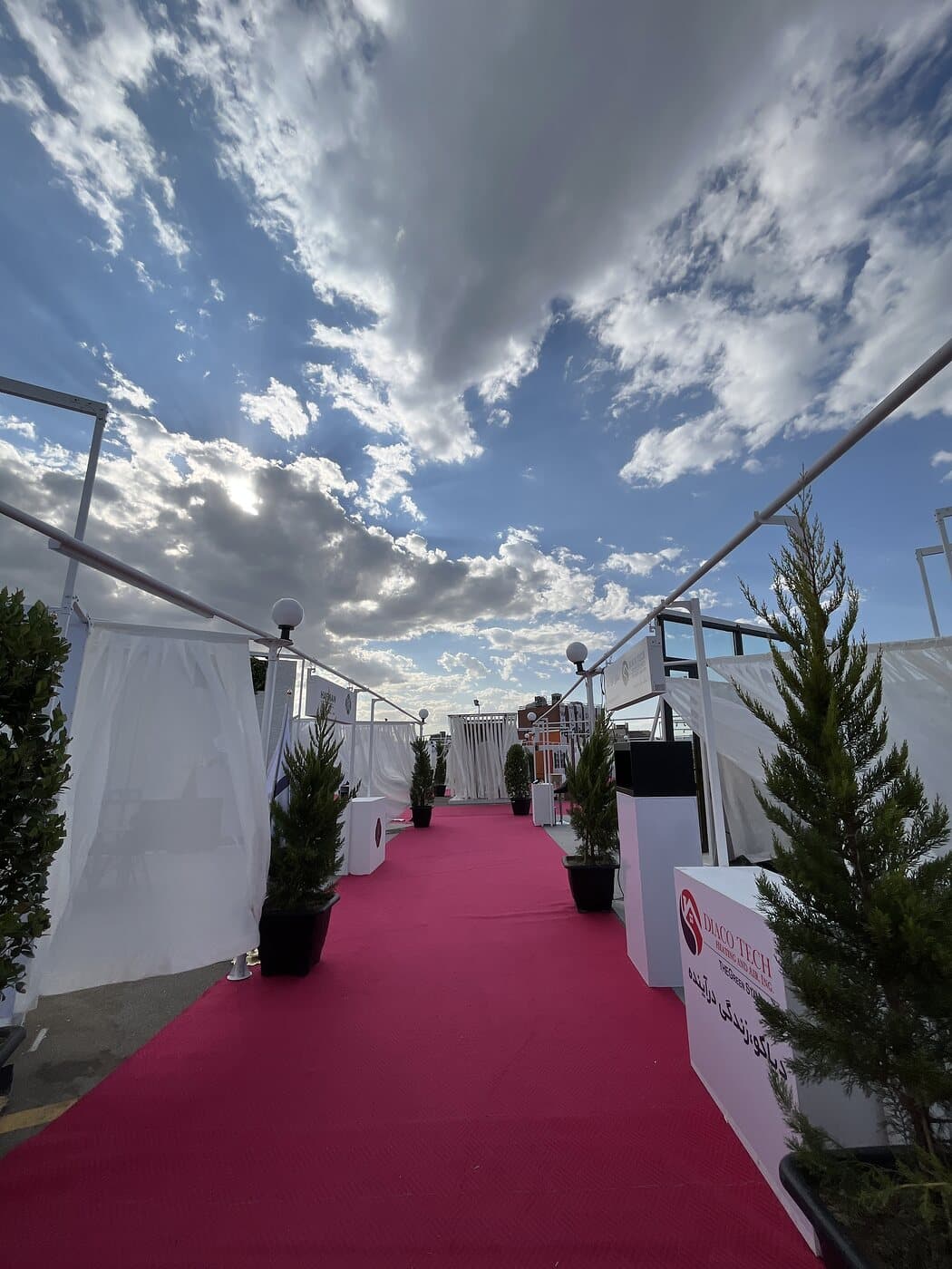 The route drawn in red carpet between the pavilions, under a high sky — WINDOW SCENE, Mashhad 2023